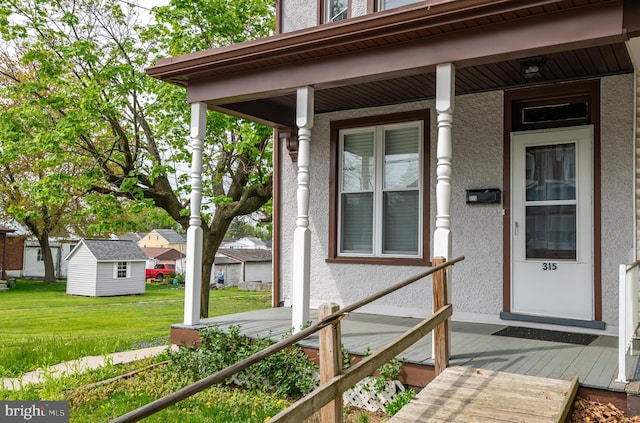 view of exterior entry featuring covered porch, stucco siding, and a yard