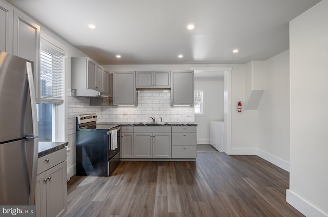 kitchen with stainless steel appliances, dark countertops, washing machine and dryer, and dark wood-type flooring