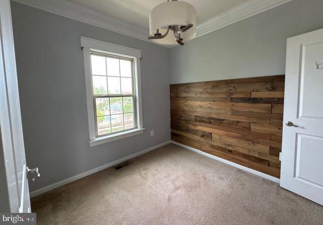 unfurnished room featuring carpet flooring, wooden walls, an inviting chandelier, visible vents, and ornamental molding