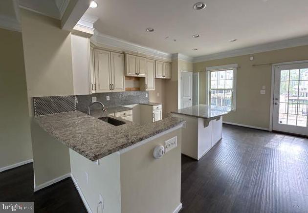 kitchen with light stone counters, a sink, plenty of natural light, a peninsula, and ornamental molding