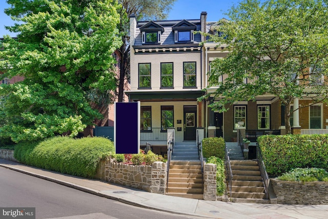 second empire-style home with a porch, brick siding, mansard roof, and stairway