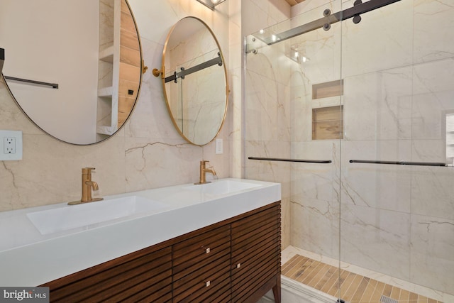 bathroom featuring a sink, tile walls, double vanity, and a marble finish shower