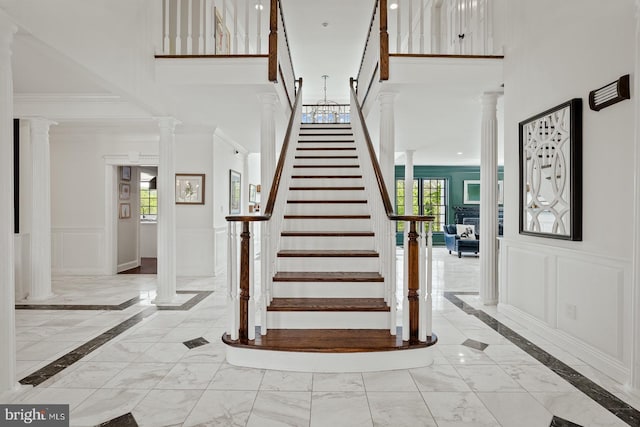stairs with ornate columns, a high ceiling, marble finish floor, and a decorative wall