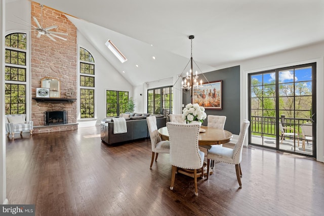 dining area featuring high vaulted ceiling, a stone fireplace, ceiling fan with notable chandelier, baseboards, and wood finished floors