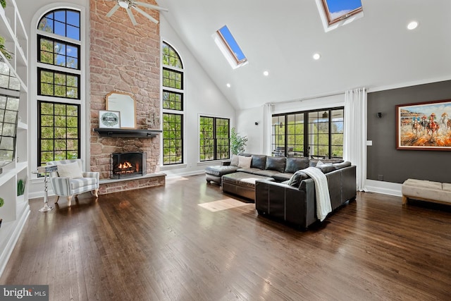 living room featuring ceiling fan, a fireplace, high vaulted ceiling, wood finished floors, and a skylight