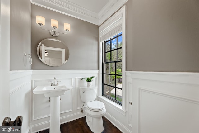half bathroom featuring wainscoting, wood finished floors, toilet, ornamental molding, and a decorative wall