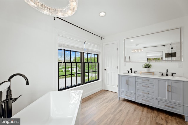 interior space with a sink, a soaking tub, double vanity, and wood finished floors