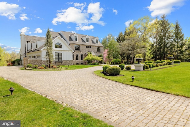 view of front facade featuring curved driveway, board and batten siding, a front yard, and stone siding