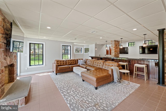 tiled living room with bar, a stone fireplace, baseboards, a drop ceiling, and recessed lighting