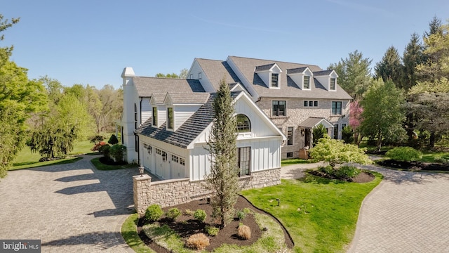 view of front of house featuring board and batten siding, a garage, decorative driveway, a front lawn, and stone siding