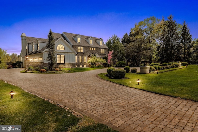 view of front of home with board and batten siding, a chimney, a front yard, curved driveway, and stone siding