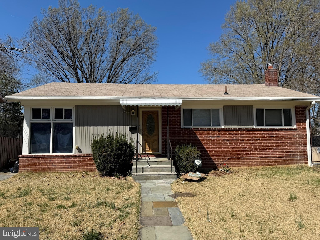 ranch-style house with brick siding, a shingled roof, a front lawn, and a chimney
