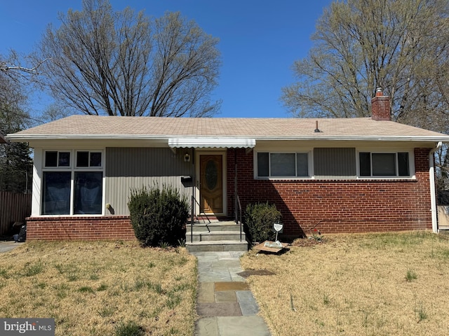 ranch-style house with brick siding, a shingled roof, a front lawn, and a chimney