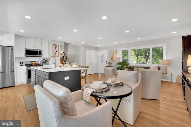 kitchen with a kitchen island with sink, open floor plan, white cabinets, a sink, and appliances with stainless steel finishes