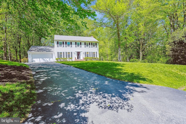 colonial house with a garage, a chimney, a front yard, and aphalt driveway