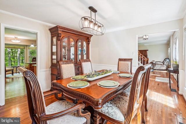 dining area with light wood-style floors, stairs, crown molding, and wainscoting