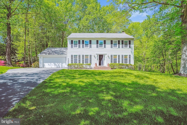 colonial home with an attached garage, a front yard, driveway, and a chimney