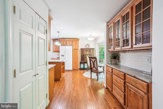 kitchen featuring backsplash, glass insert cabinets, white fridge with ice dispenser, and light wood-style floors