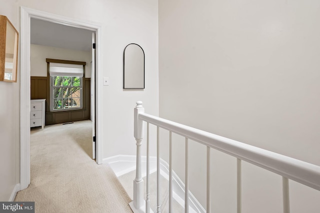 hall with an upstairs landing, light carpet, and baseboards