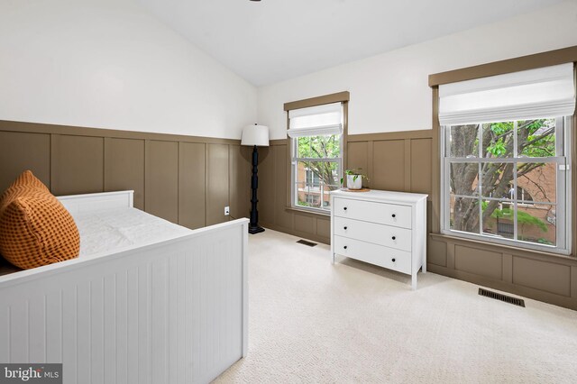 bedroom with a decorative wall, light colored carpet, lofted ceiling, and wainscoting