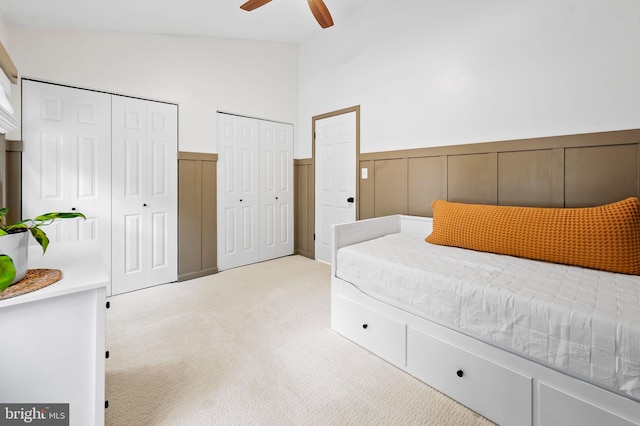 bedroom with light colored carpet, two closets, a wainscoted wall, and ceiling fan