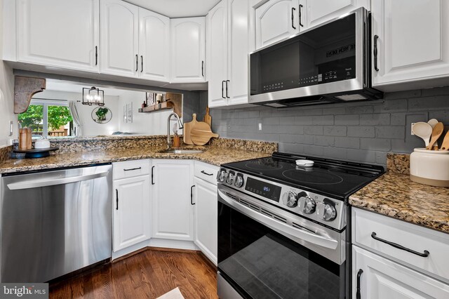 kitchen featuring appliances with stainless steel finishes, a sink, dark wood-style flooring, and light stone countertops
