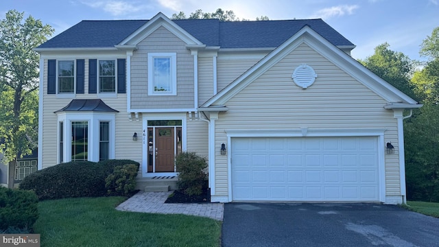 traditional-style home featuring a garage, aphalt driveway, a front yard, and a shingled roof