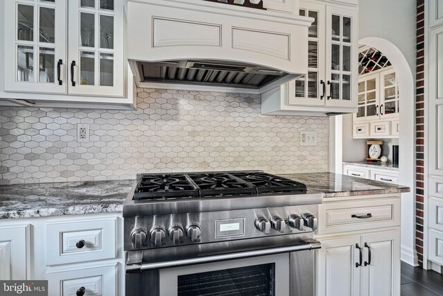 kitchen with high end stove, decorative backsplash, custom exhaust hood, and glass insert cabinets