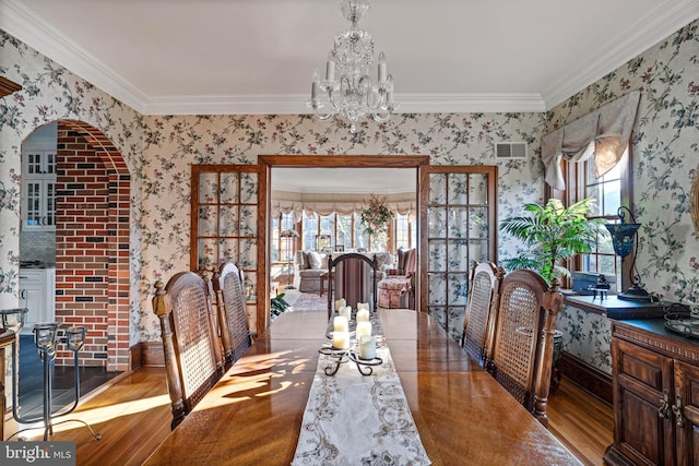 dining area featuring visible vents, crown molding, an inviting chandelier, wood finished floors, and wallpapered walls