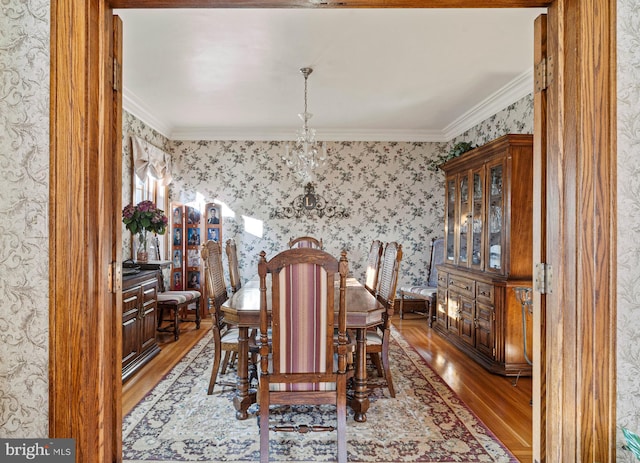 dining area featuring ornamental molding, wallpapered walls, wood finished floors, and a chandelier