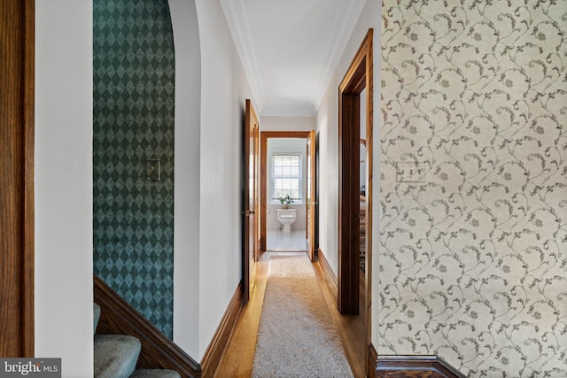 corridor featuring carpet floors, wallpapered walls, ornamental molding, and baseboards