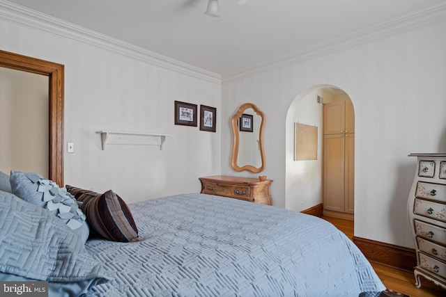 bedroom with crown molding, arched walkways, baseboards, and wood finished floors