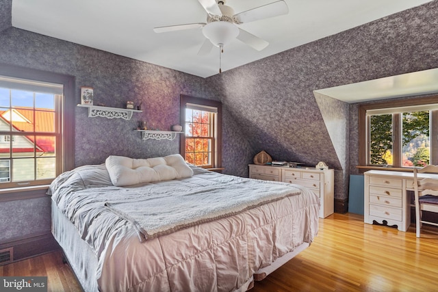 bedroom featuring ceiling fan, wallpapered walls, wood finished floors, and visible vents