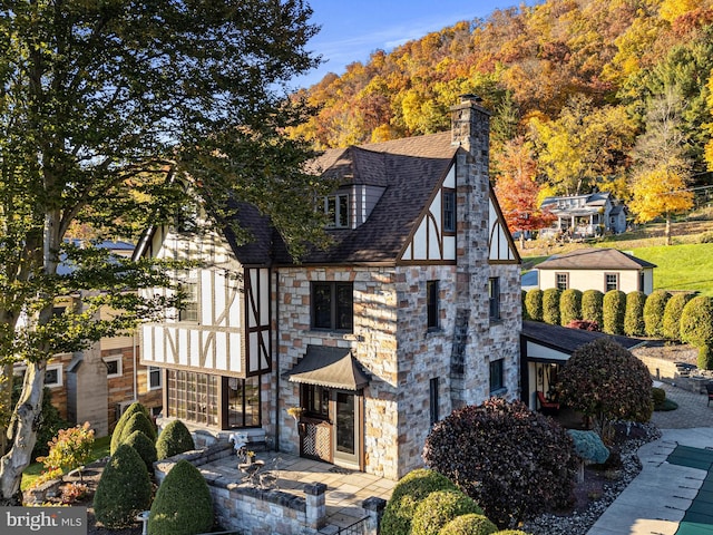 view of side of home featuring a chimney, a patio area, and stone siding