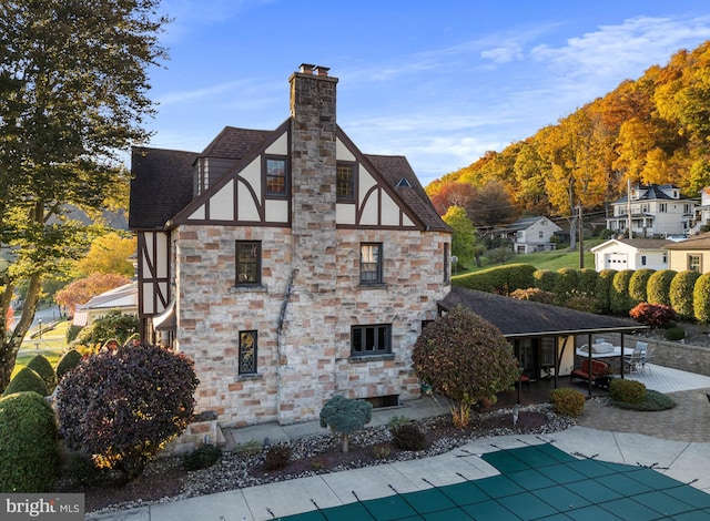 view of home's exterior with a chimney, a patio area, a shingled roof, a covered pool, and stone siding