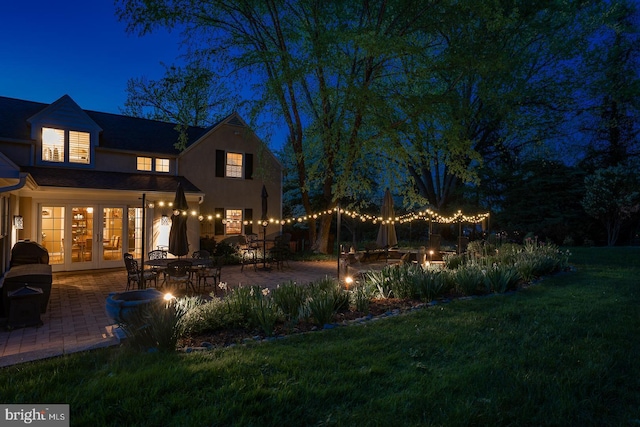 back of house at twilight with a lawn, a patio, french doors, and stucco siding