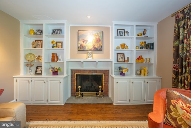 living room with a brick fireplace, wood finished floors, and built in shelves