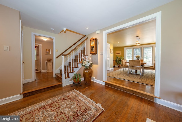 foyer featuring baseboards, wood finished floors, and stairway