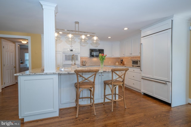 kitchen with black microwave, paneled refrigerator, white cabinets, tasteful backsplash, and light stone counters