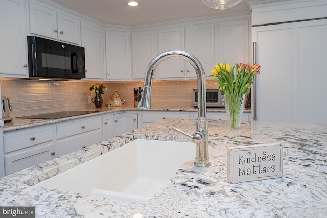 kitchen with tasteful backsplash, light stone countertops, a sink, white cabinets, and black appliances