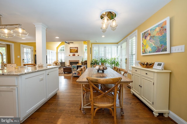 dining area featuring a ceiling fan, decorative columns, dark wood-type flooring, and a fireplace
