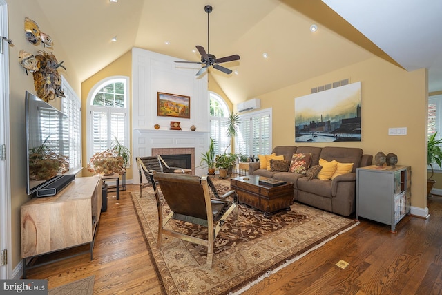 living area featuring wood finished floors, a ceiling fan, a brick fireplace, and a wall unit AC