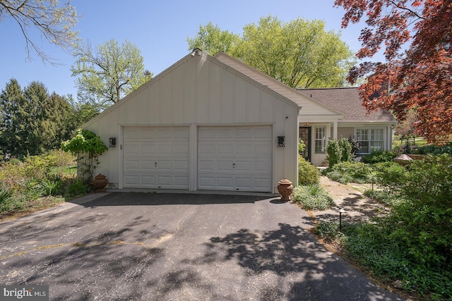 view of front facade with board and batten siding, an attached garage, roof with shingles, and aphalt driveway