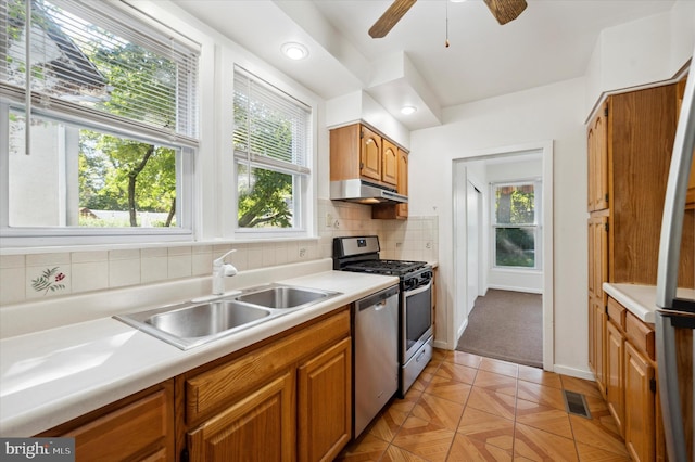 kitchen featuring brown cabinetry, light countertops, under cabinet range hood, a sink, and appliances with stainless steel finishes