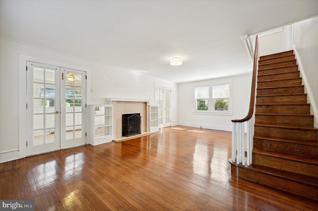 unfurnished living room featuring french doors, a fireplace, wood finished floors, baseboards, and stairs