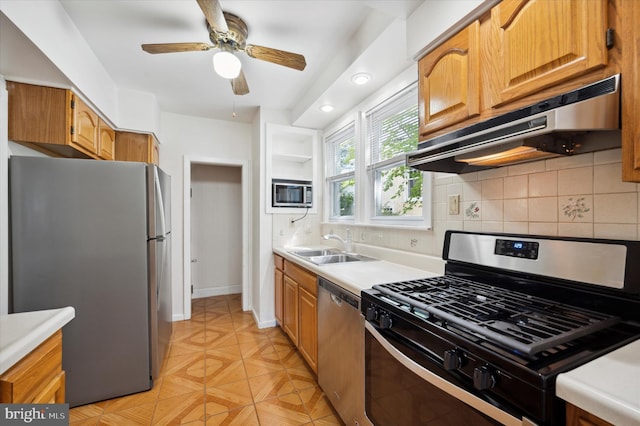 kitchen with light countertops, under cabinet range hood, tasteful backsplash, a sink, and appliances with stainless steel finishes