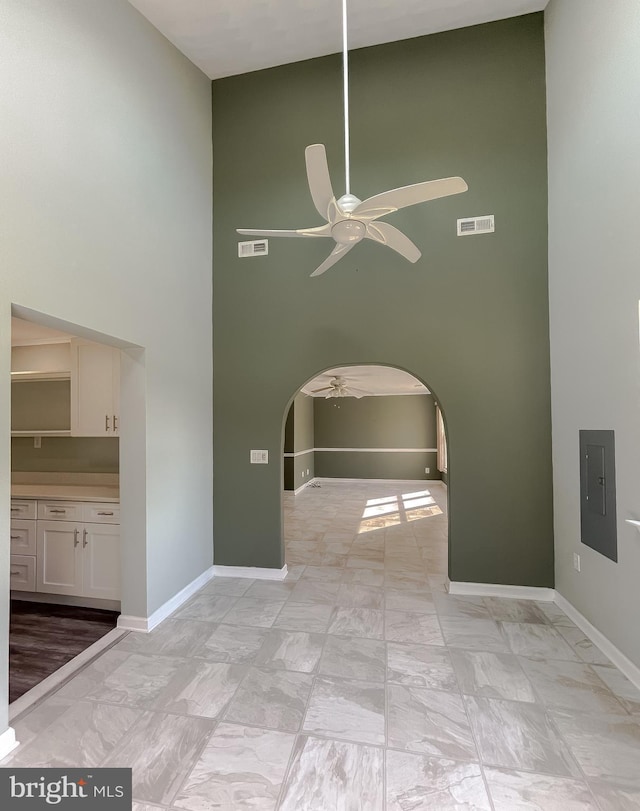 spare room with visible vents, a towering ceiling, arched walkways, electric panel, and a ceiling fan