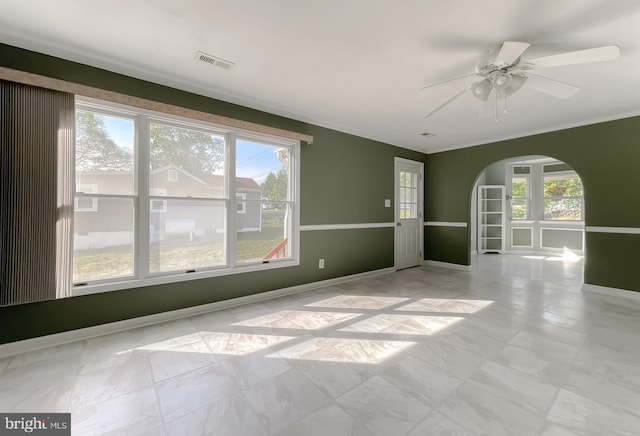 empty room featuring visible vents, crown molding, baseboards, ceiling fan, and arched walkways