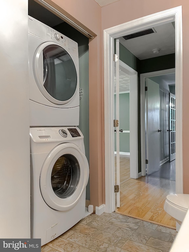 clothes washing area with laundry area, baseboards, stone finish flooring, stacked washer / dryer, and visible vents