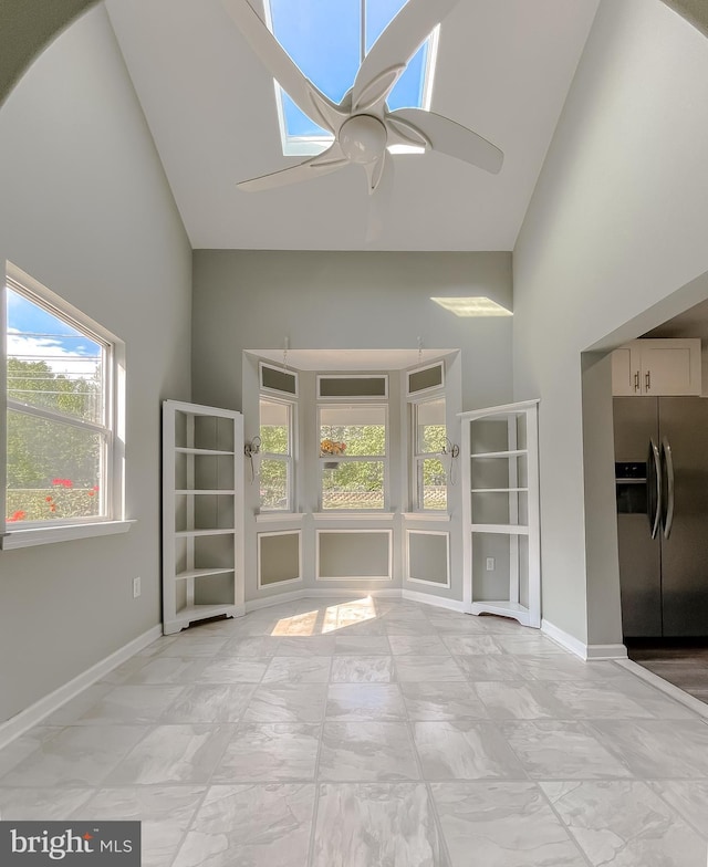 unfurnished living room with marble finish floor, a skylight, a healthy amount of sunlight, and high vaulted ceiling